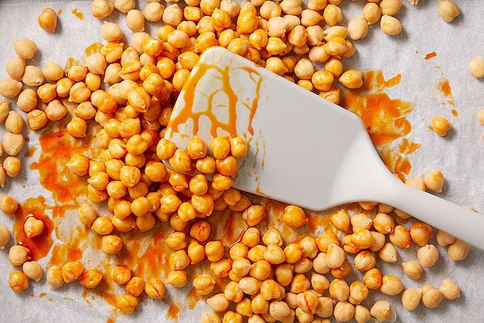 Overhead horizontal image of chickpeas being tossed with chili crisp sauce using a spatula.