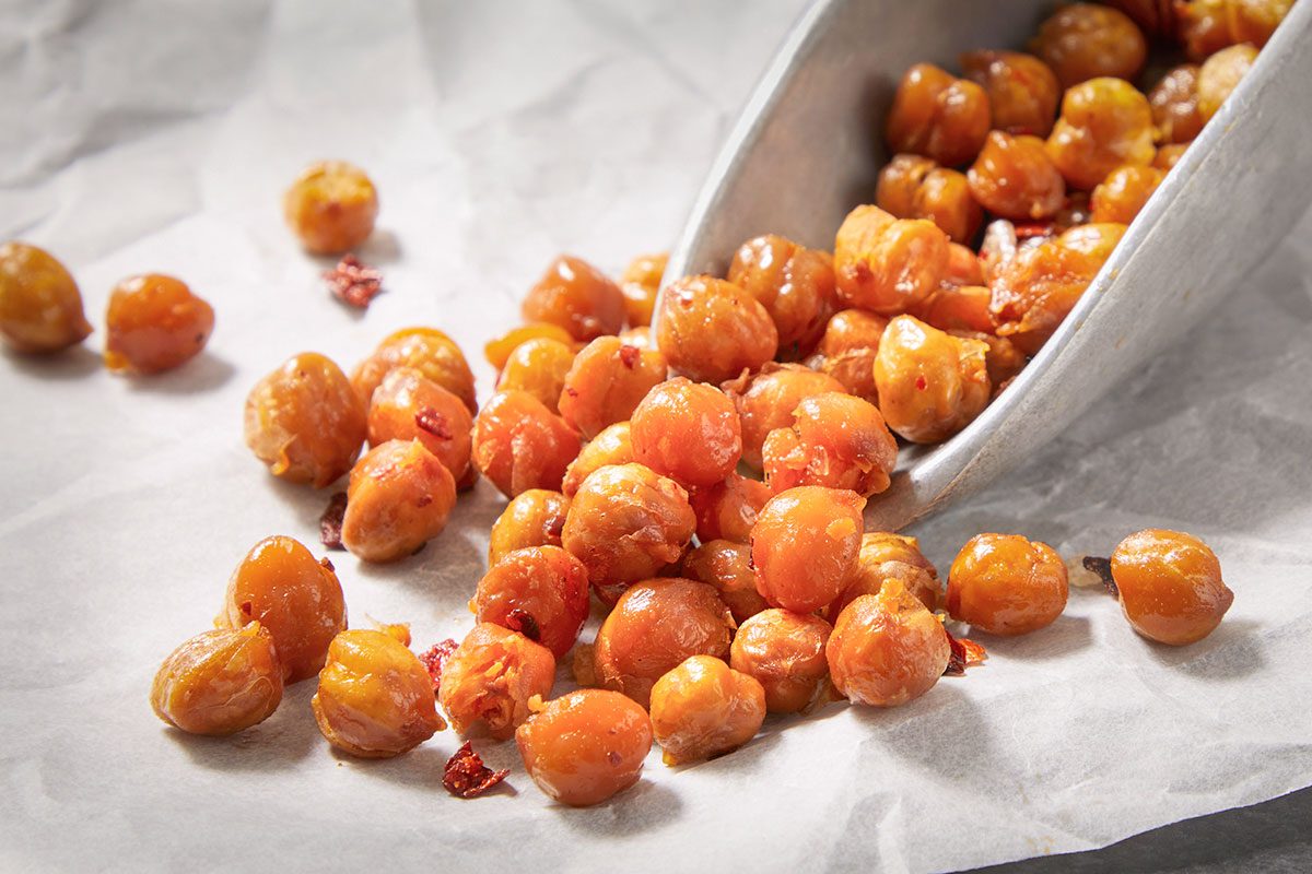 Overhead horizontal close-up of chili crisp chickpeas spilling from parchment paper showing texture and seasoning.