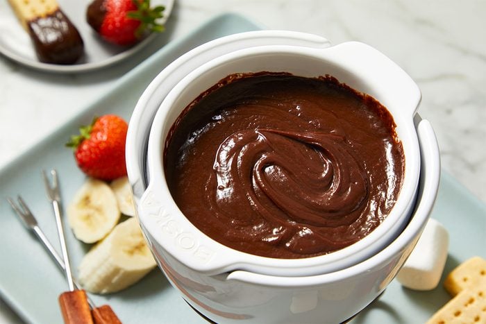 3/4 overhead view of the Peanut Butter Chocolate Fondue pot filled with smooth, glossy chocolate-peanut butter fondue, with dipping items including fruit and cake placed nearby.