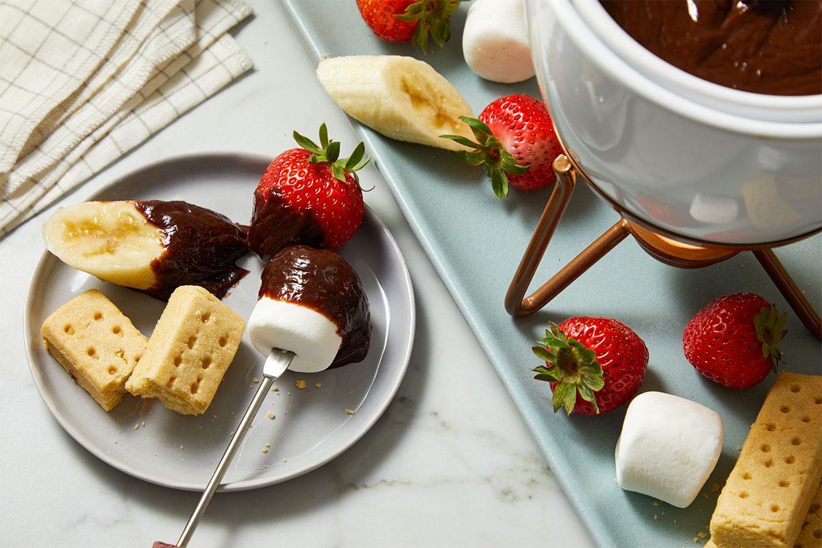 3/4 shot of the Fondue setup with strawberries, banana slices, marshmallows, and cubes of cake arranged around the pot, ready for dipping.