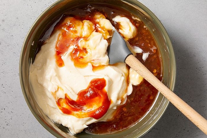 Overhead horizontal image of mayonnaise and chili sauces being mixed together to create bang bang sauce.