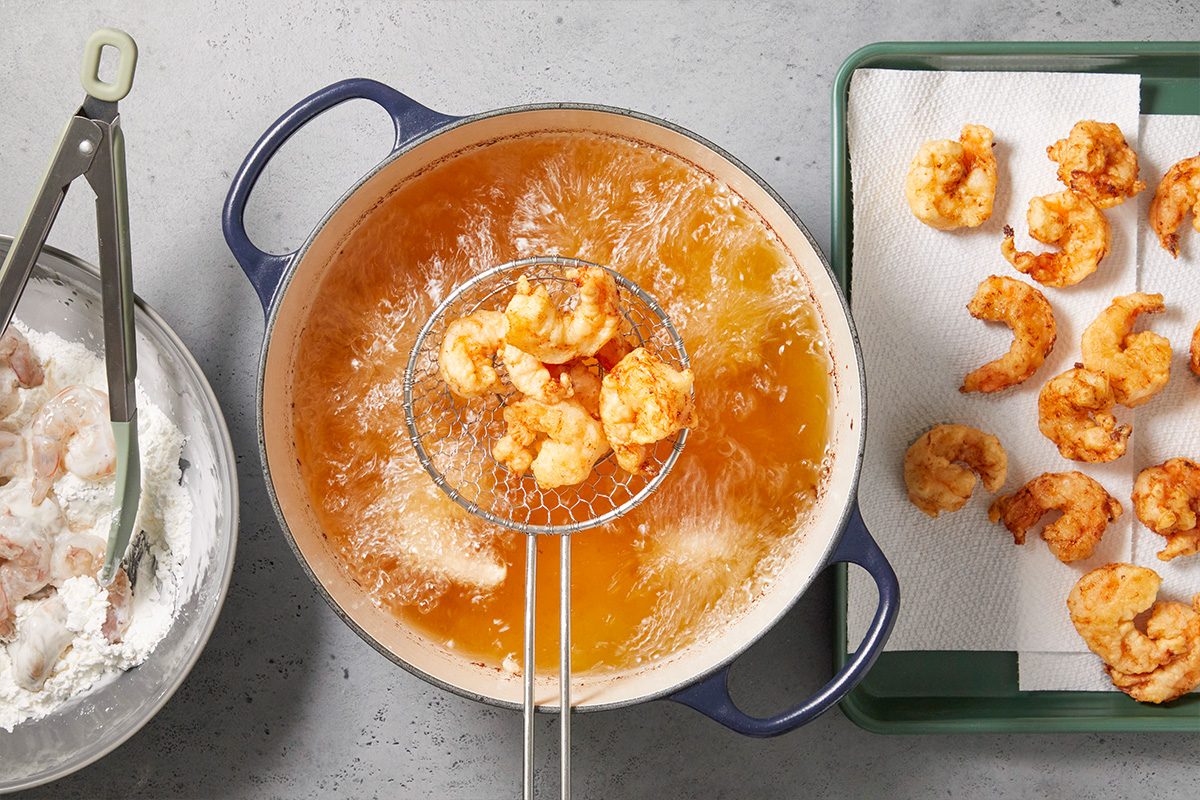 Overhead horizontal image of shrimp being fried in hot oil until golden brown.