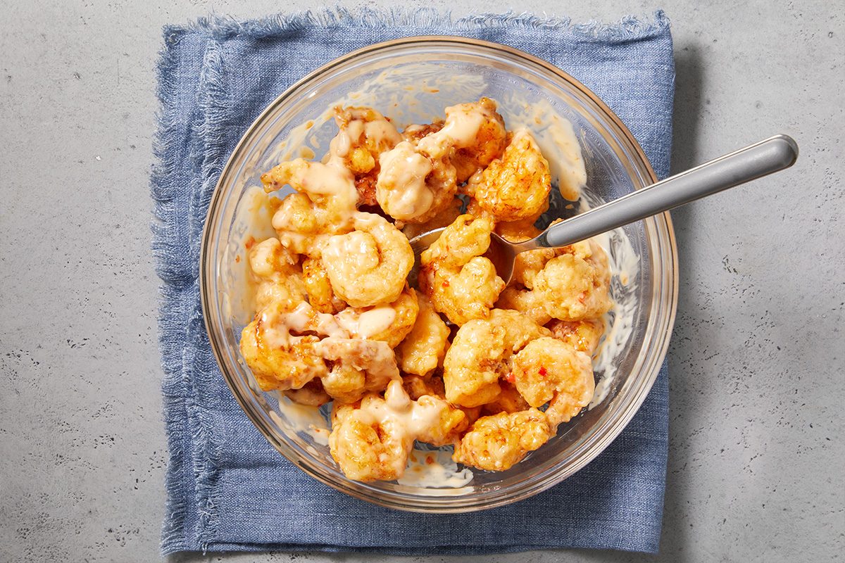 Overhead horizontal image of fried shrimp tossed in creamy bang bang sauce in a mixing bowl.