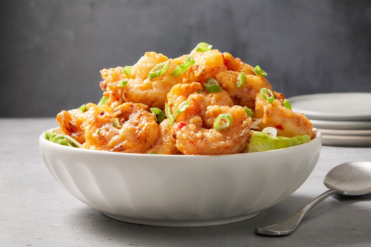 Eye-level horizontal image of bang bang shrimp served in a bowl with sauce and garnish.