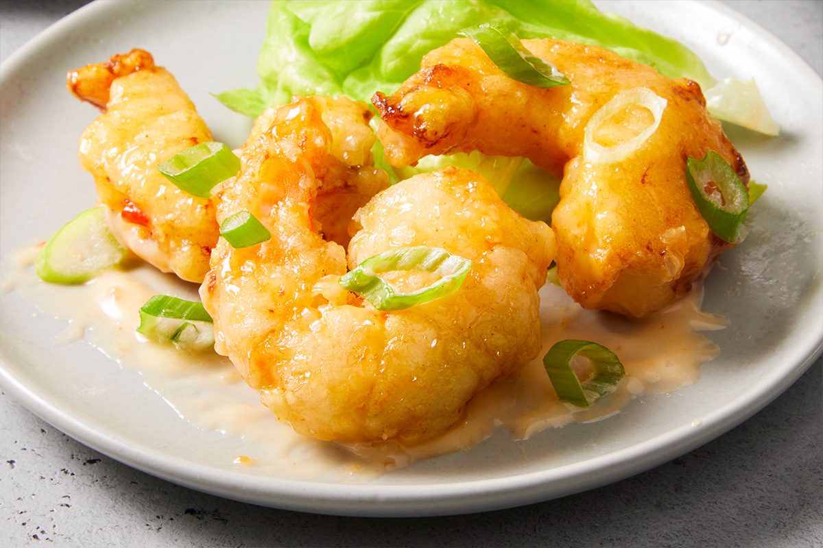 Eye-level horizontal close-up of bang bang shrimp on a plate showing crispy coating and creamy sauce.