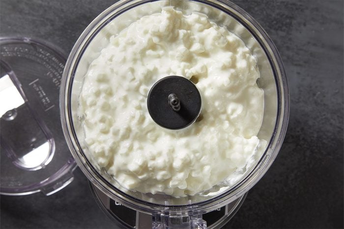 Overhead shot of cottage cheese in a food processor bowl before blending, set on a dark countertop.