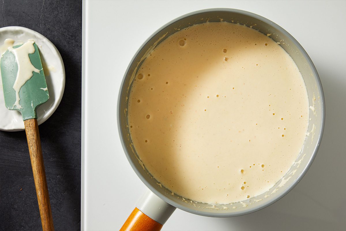 Overhead shot of smooth sauce in a saucepan, with a spatula resting nearby.