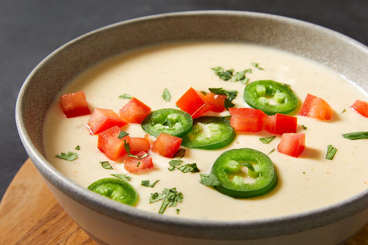 Close-up shot of creamy Cottage Cheese Queso topped with chopped tomatoes and sliced jalapeños.