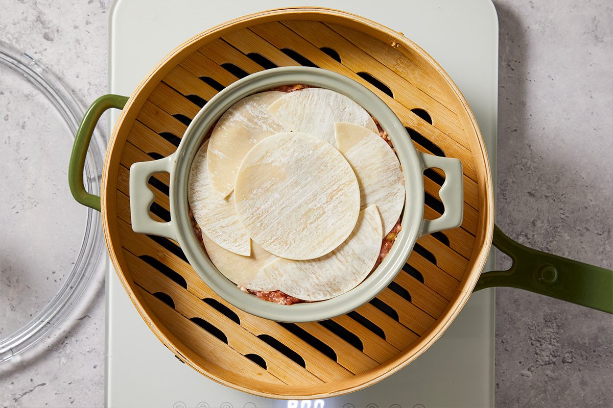 Overhead image showing a baking dish filled with layered wonton wrappers placed inside a steamer basket before cooking the dumpling lasagna.