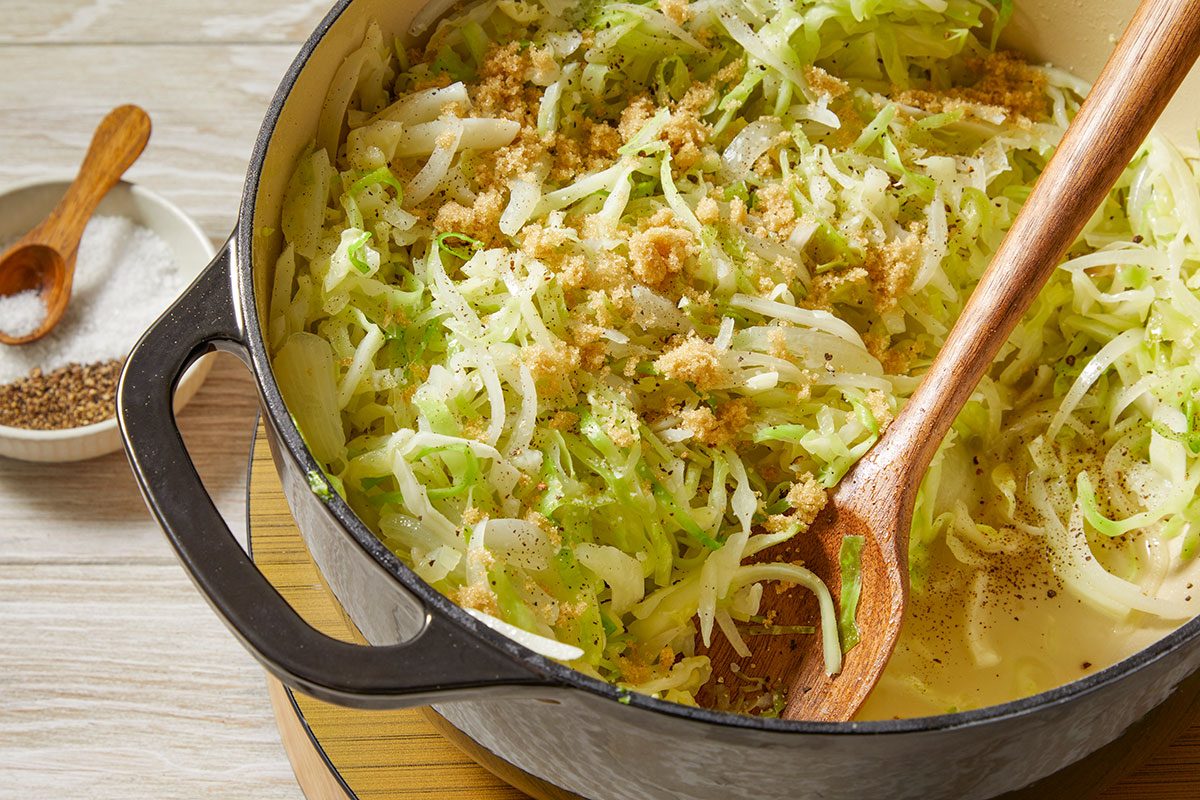 Overhead horizontal image of sliced cabbage and onions cooking in a Dutch oven with butter and oil.