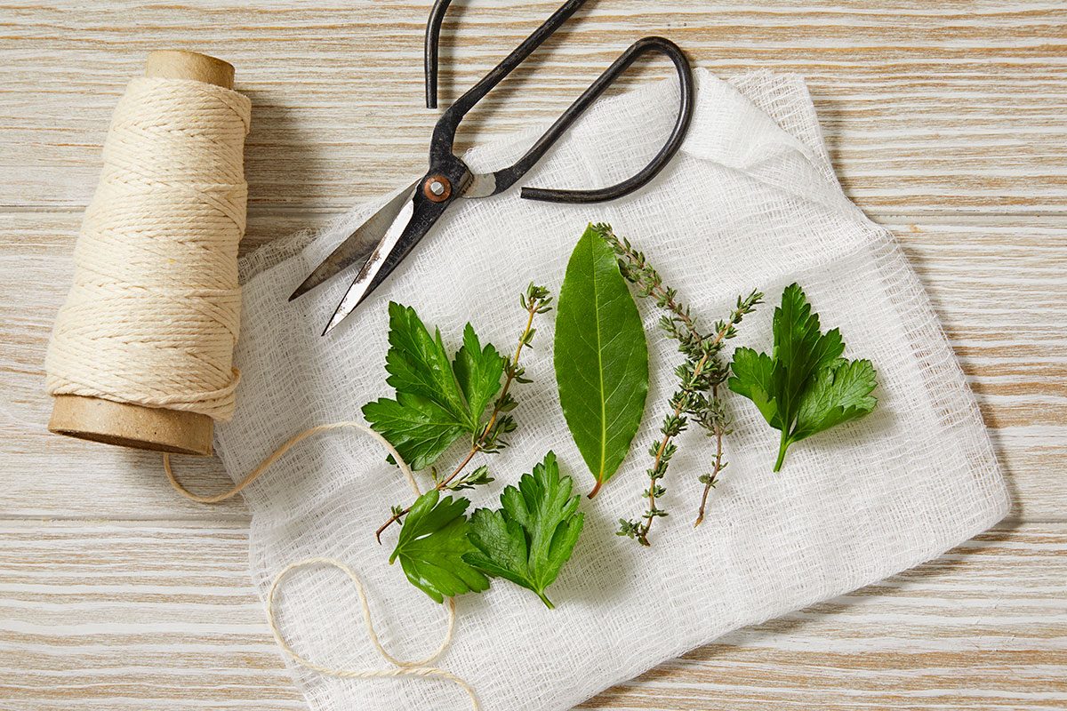 Overhead horizontal image of fresh herbs including parsley and thyme arranged on a cloth with kitchen tools.