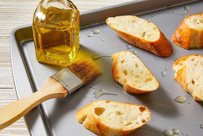 Overhead horizontal image of sliced baguette brushed with olive oil on a sheet pan.