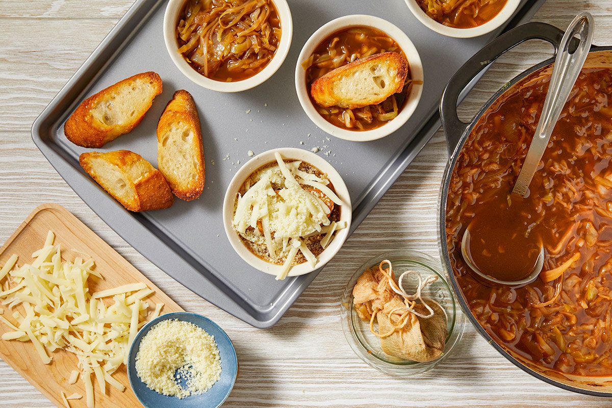 Overhead horizontal image of soup setup with bowls, toasted bread, shredded cheese, and prepared soup.