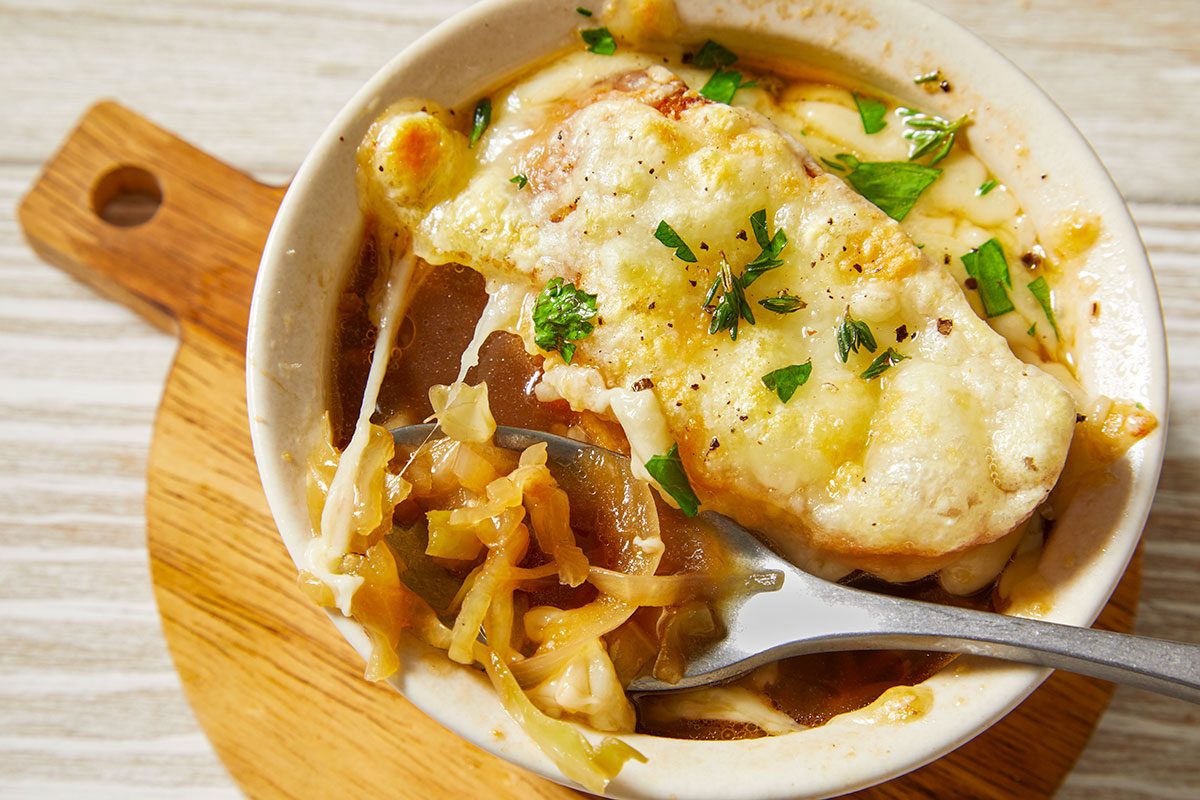 Overhead horizontal close-up of French onion cabbage soup with melted cheese and bread topping being scooped.