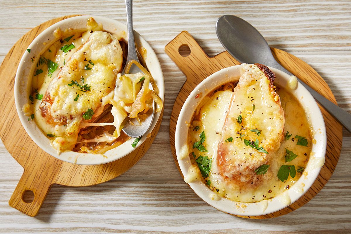 Overhead horizontal image of two bowls of French onion cabbage soup topped with melted cheese and herbs.