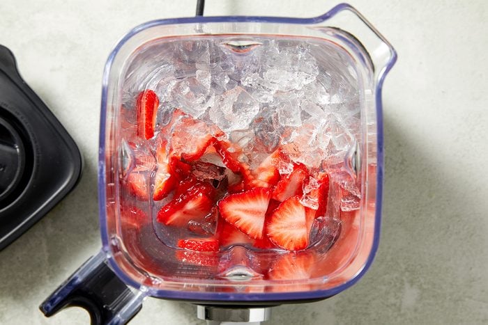 Overhead step-by-step image showing crushed ice and sliced strawberries inside a blender jar
