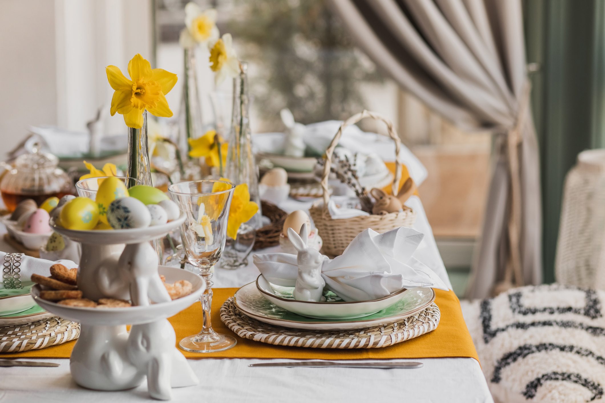 Setting table for Easter dinner with candles, flowers, multicolored eggs and ceramic plates in shape Easter bunny.