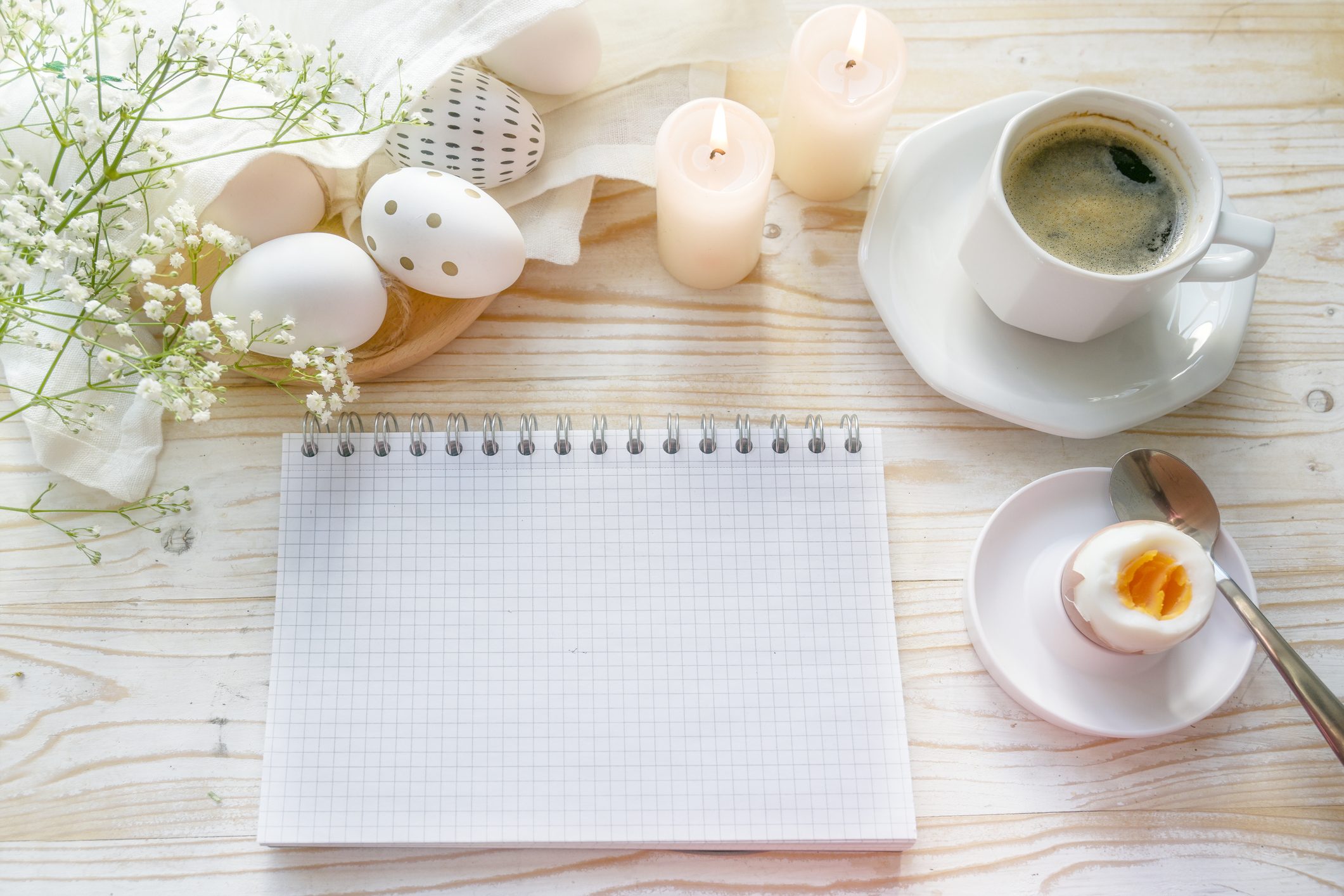 Blank spiral notepad on an Easter table with eggs, coffee, candles and flowers, mock-up for a holiday to-do list, invitation or save the date, top view from above, copy space