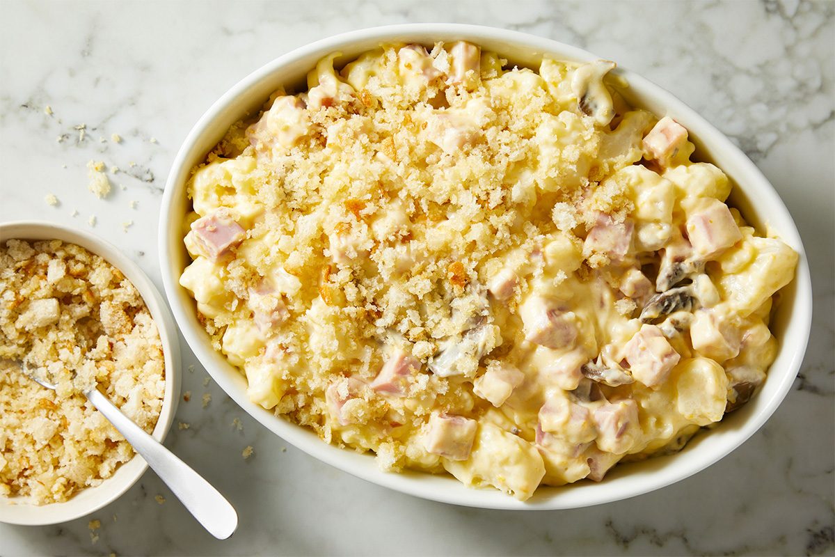Overhead shot of the ham and cauliflower mixture transferred into an oval baking dish and evenly topped with buttery breadcrumbs.