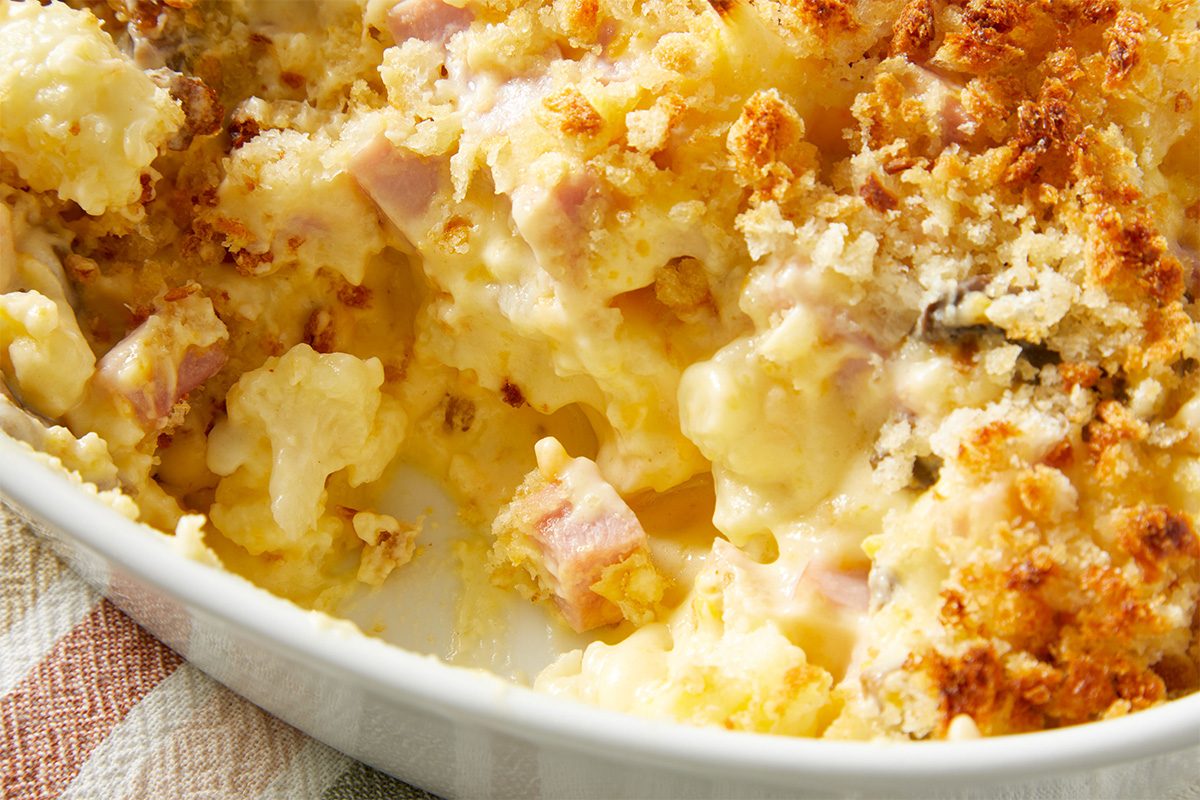 Close-up shot of the baked Cauliflower Ham Casserole, highlighting the creamy interior and browned breadcrumb crust.