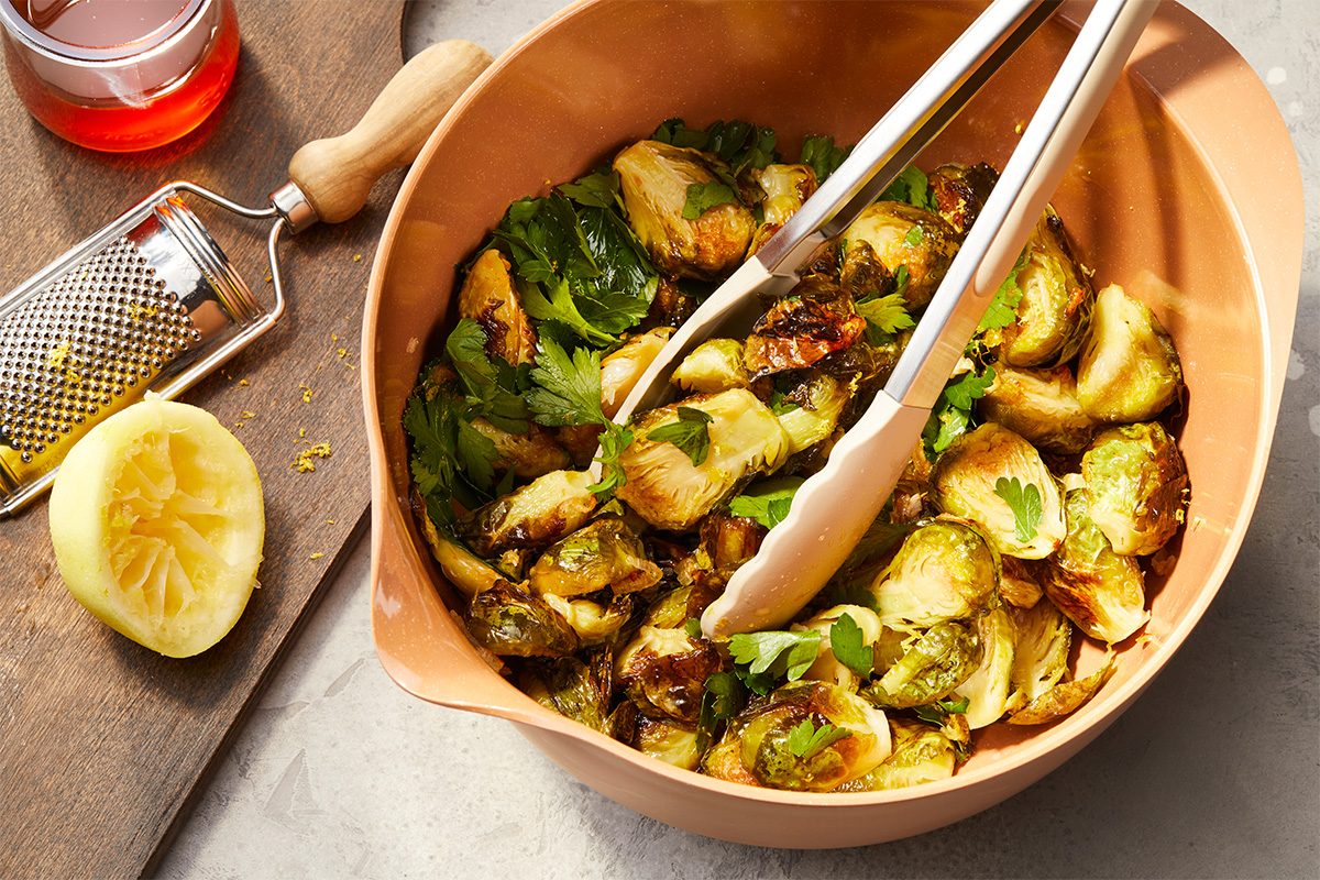 Overhead horizontal image of roasted Brussels sprouts tossed with parsley, lemon, and hot honey in a serving bowl.