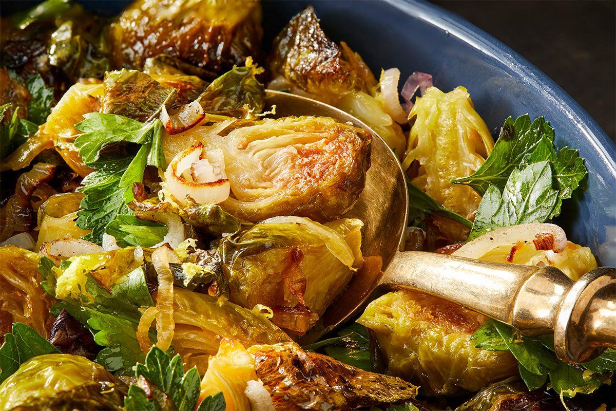 Overhead horizontal close-up of roasted Brussels sprouts showing caramelized edges, herbs, and glossy hot honey coating.