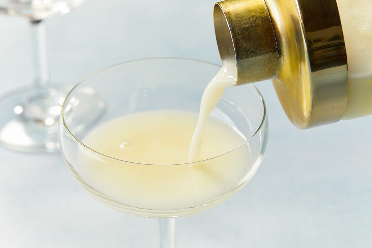 Overhead image of a Lemon Cream Martini mixture being poured from a cocktail shaker into a coupe glass.