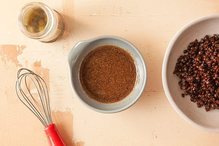 Overhead horizontal image of vinaigrette dressing with whisk alongside cooked black lentils on a neutral background.