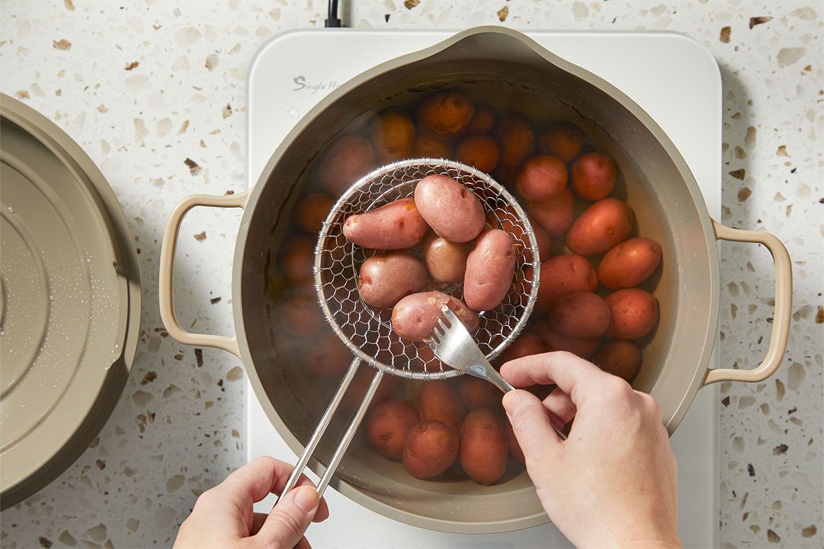 Overhead shot of small red potatoes boiling in a pot of water, with a strainer lifting them partially above the surface.