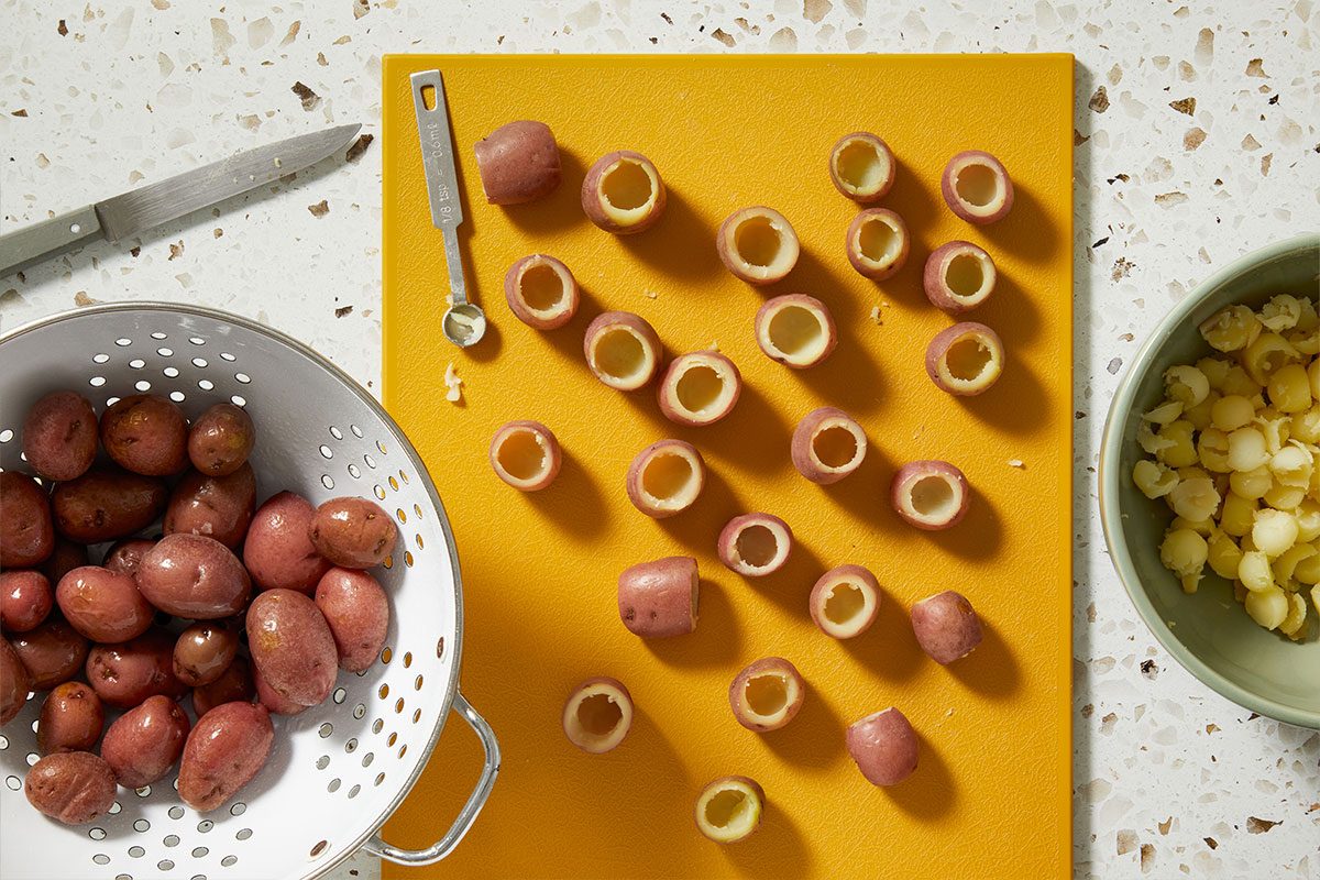 Overhead shot of cooked mini potatoes arranged on a cutting board, with potato halves and scooping tools nearby.