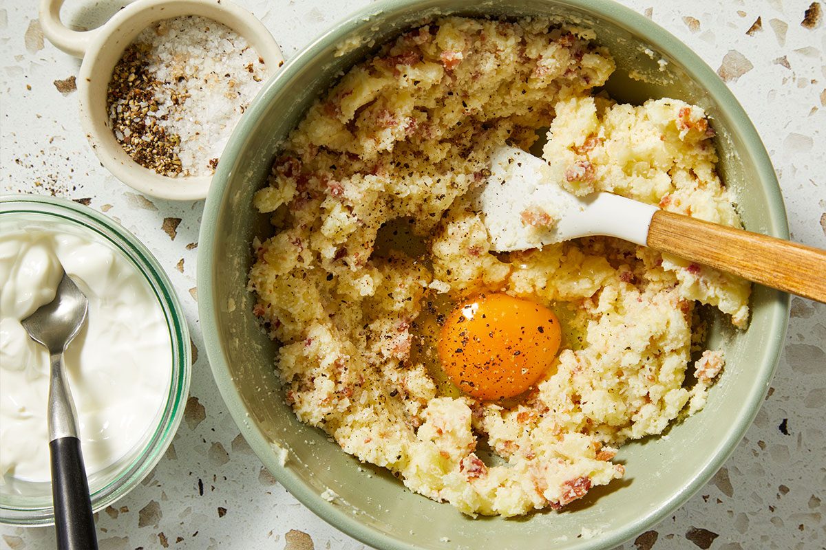 Overhead shot of mashed potato mixture with an egg added to the center, ready to be mixed for stuffing.