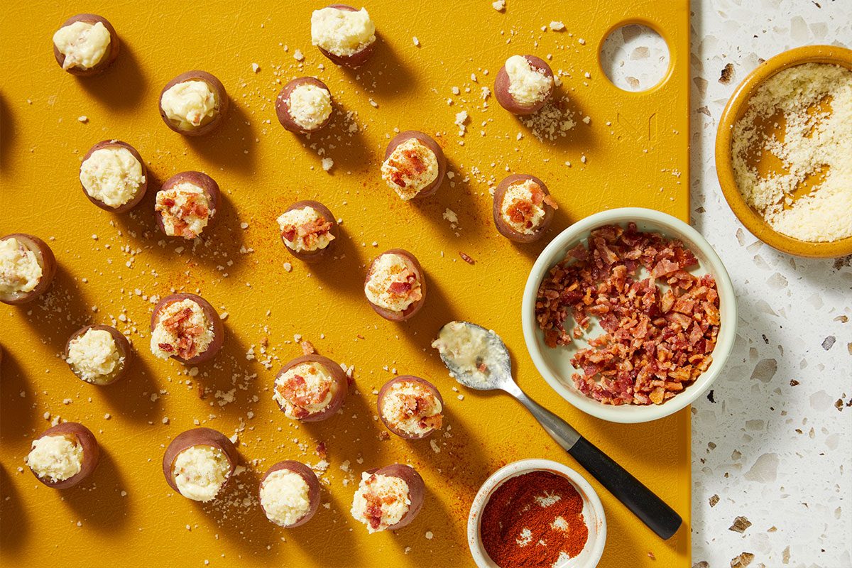 Overhead shot of mini potato shells arranged on a baking tray, each filled with mashed potato mixture and topped with cheese.