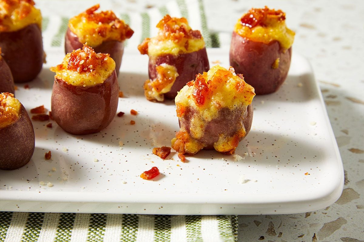 Close up shot of Stuffed Baby Red Potatoes arranged on a platter, topped with melted cheese and garnished with herbs.