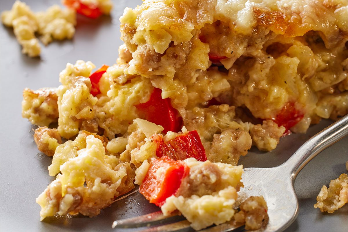 Close-up shot of Monterey Sausage Pie on a plate, showing scrambled eggs, sausage, melted cheese, and red bell peppers, with a fork beside it;