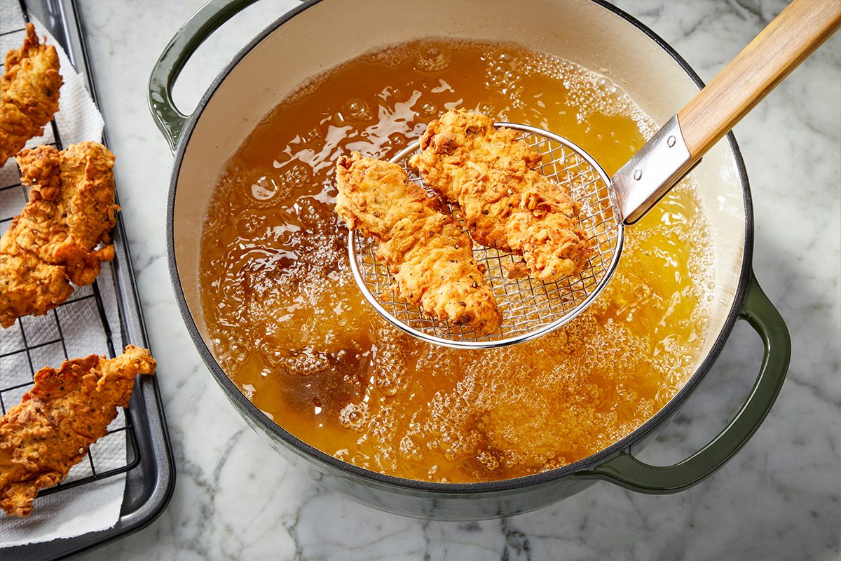 Overhead horizontal image of breaded chicken tenders frying in hot oil in a Dutch oven.