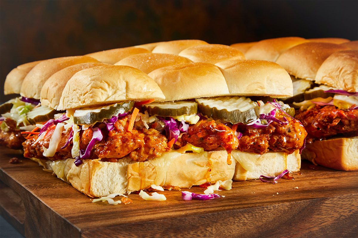 Overhead horizontal image of multiple Nashville hot honey chicken sliders assembled on a cutting board.