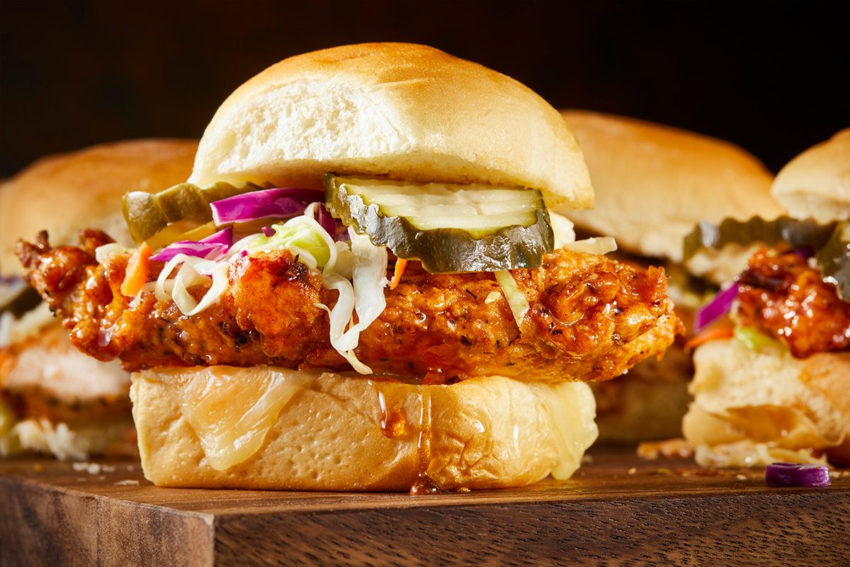Overhead horizontal close-up of a Nashville hot honey chicken slider showing crispy chicken, coleslaw, and pickles inside a soft bun.