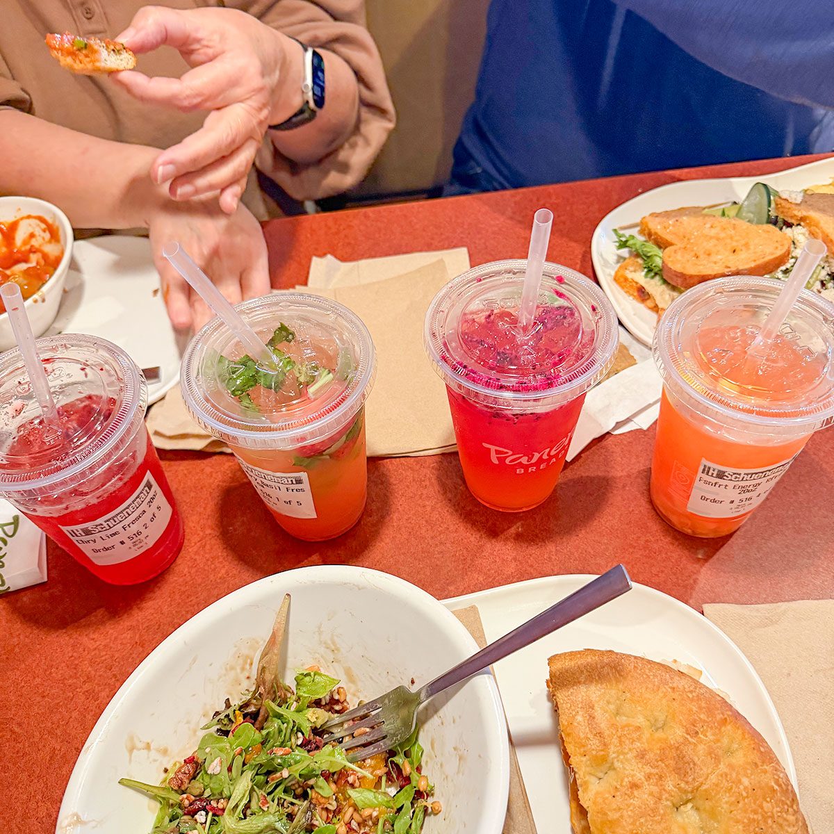 Four different flavoured drink and food in plate served on a table, Two people eating their food and drinks