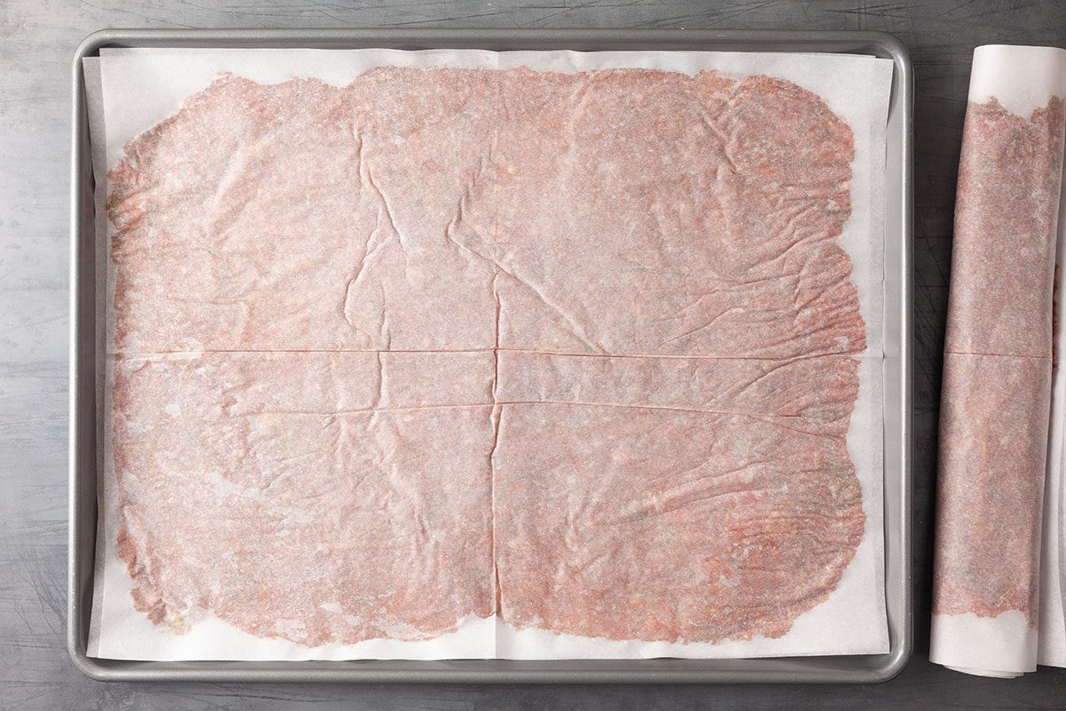 Overhead image of seasoned ground beef mixture pressed evenly onto parchment paper and rolled into a tight log shape, preparing the gyro meat for baking.