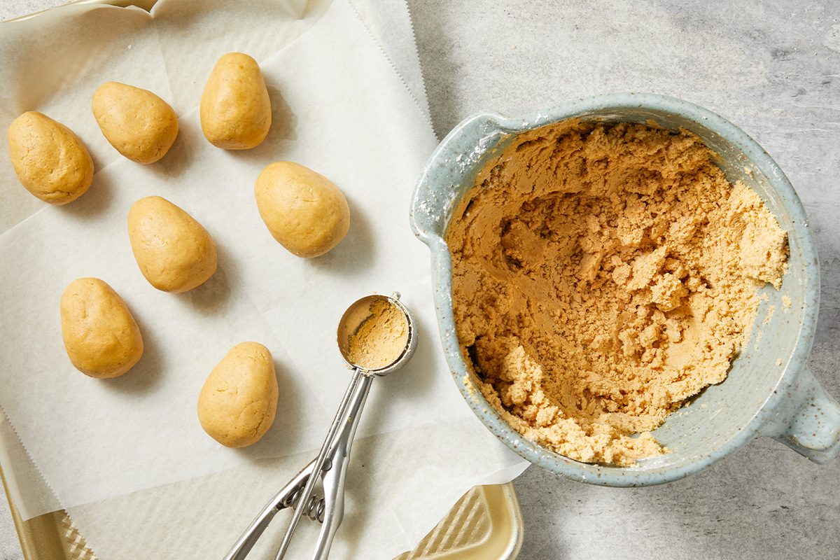 Overhead image of peanut butter filling shaped into small egg forms and arranged on parchment paper beside the mixing bowl. A cookie scoop is visible, highlighting the portioning step for uniform candy centers.