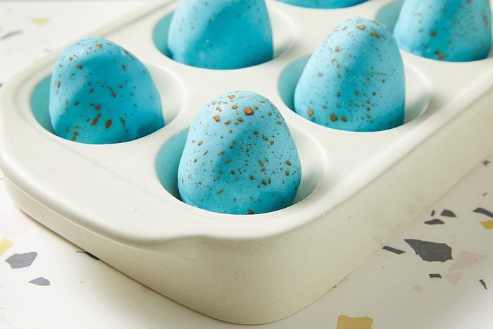 Horizontal close-up of Peanut Butter Robin Eggs nestled in a serving dish, highlighting the smooth blue coating and cocoa speckled finish. The image emphasizes texture and presentation.