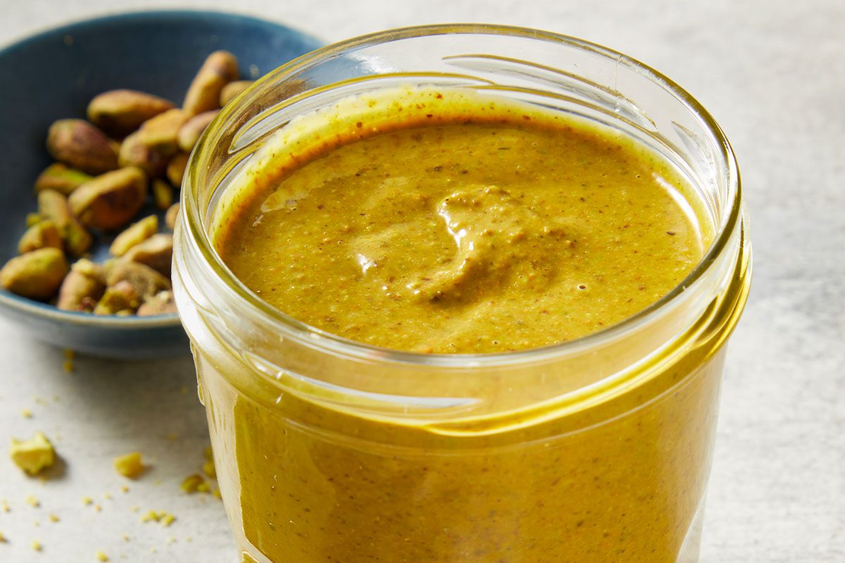Vertical overhead image of freshly blended Pistachio Butter spooned into a glass jar. The smooth texture and rich green color emphasize its creamy consistency and homemade appeal.