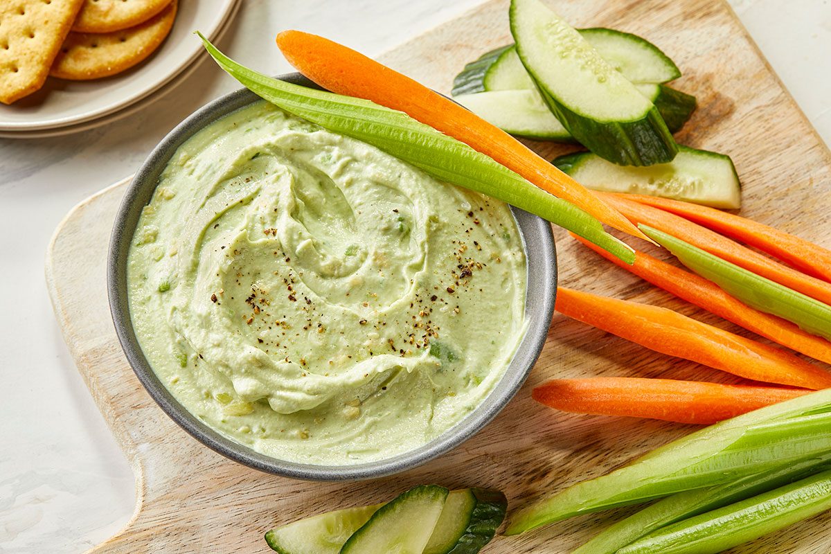 Overhead image of Ranch Avocado Yogurt Dip served with fresh carrots, celery and cucumber slices on a wooden board.