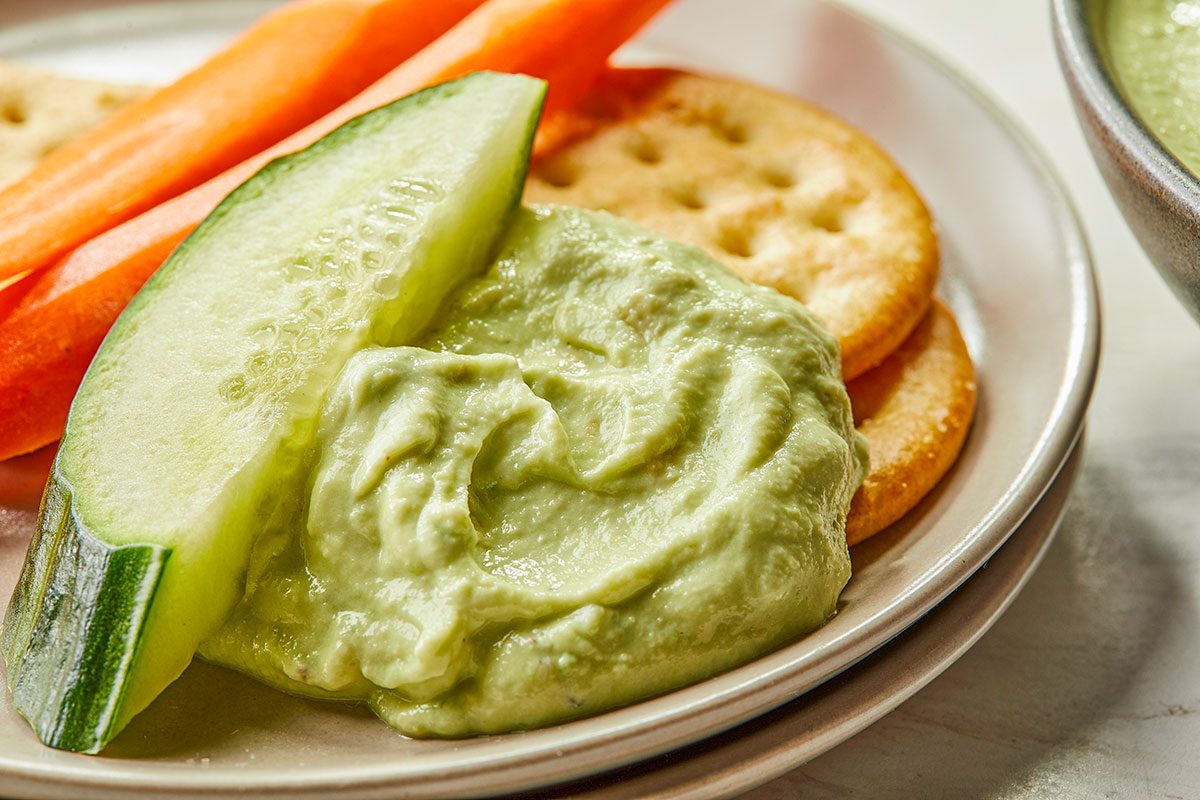 Overhead close-up of creamy Ranch Avocado Yogurt Dip served with crackers and fresh cucumber slices.