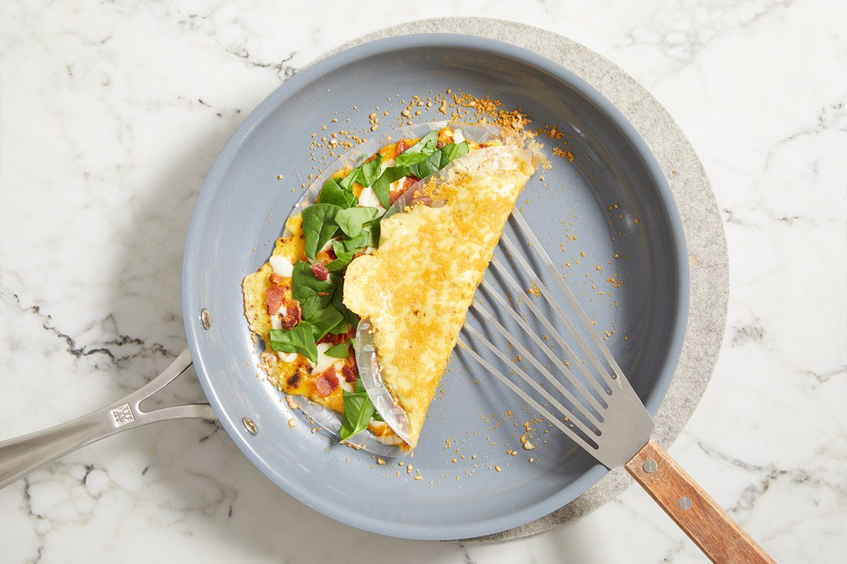 Overhead push and pulls image of Rice Paper Breakfast Pizza folded in half in a skillet with a spatula, showing crisped exterior and melted filling on a marble background.