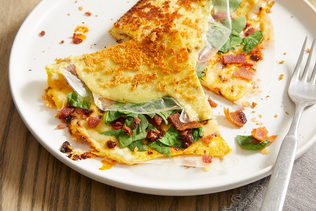Vertical push and pulls image of sliced Rice Paper Breakfast Pizza on a plate, showing detailed texture of crisped rice paper and savory filling with eggs, spinach, bacon, and melted cheeses.