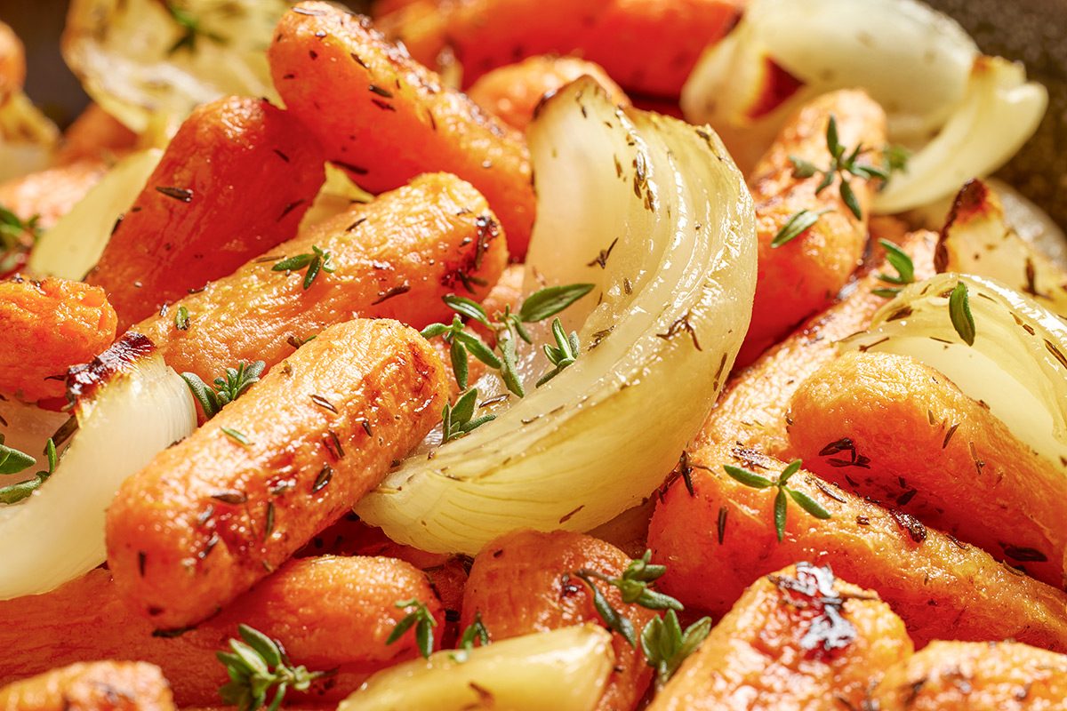 Close-up of roasted baby carrots and onion wedges garnished with fresh thyme, showing a golden-brown, caramelized texture.