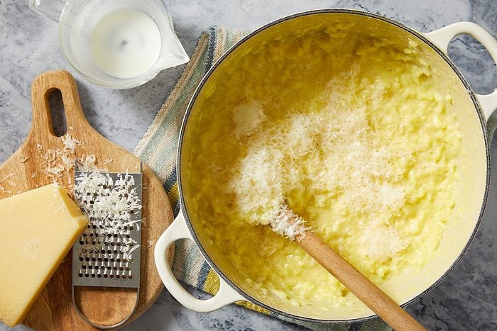 Overhead push and pulls image of grated Parmesan cheese being stirred into creamy saffron risotto in a Dutch oven to finish the dish.