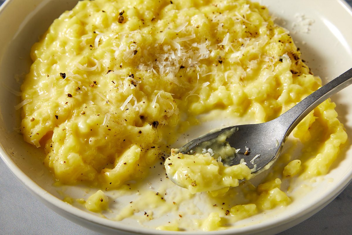 Overhead push and pulls close-up image of creamy saffron risotto in a bowl with a spoon lifting the rich golden rice.