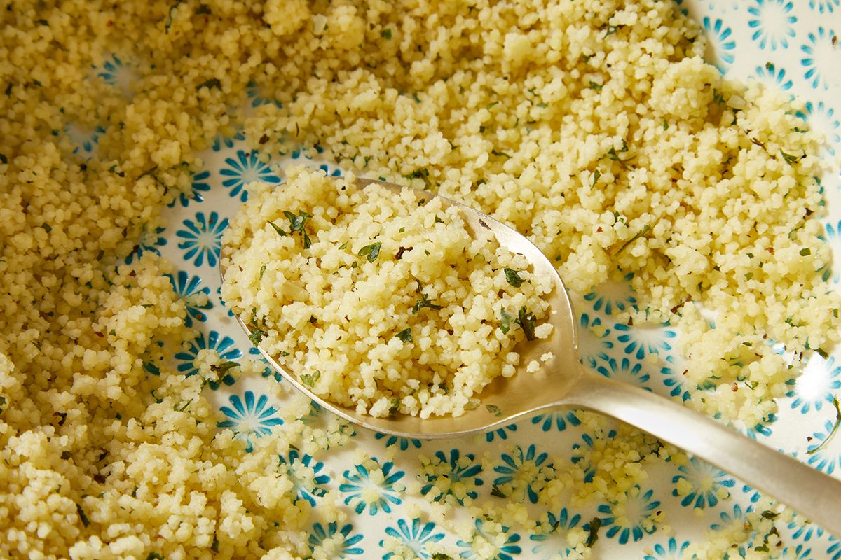 A close-up of cooked couscous being scooped with a spoon from a patterned blue and white dish.
